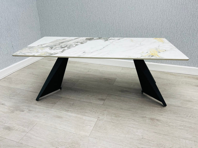 Ceramic coffee table with black legs. the ceramic top has cream and  gold colors. it is 120 cm long