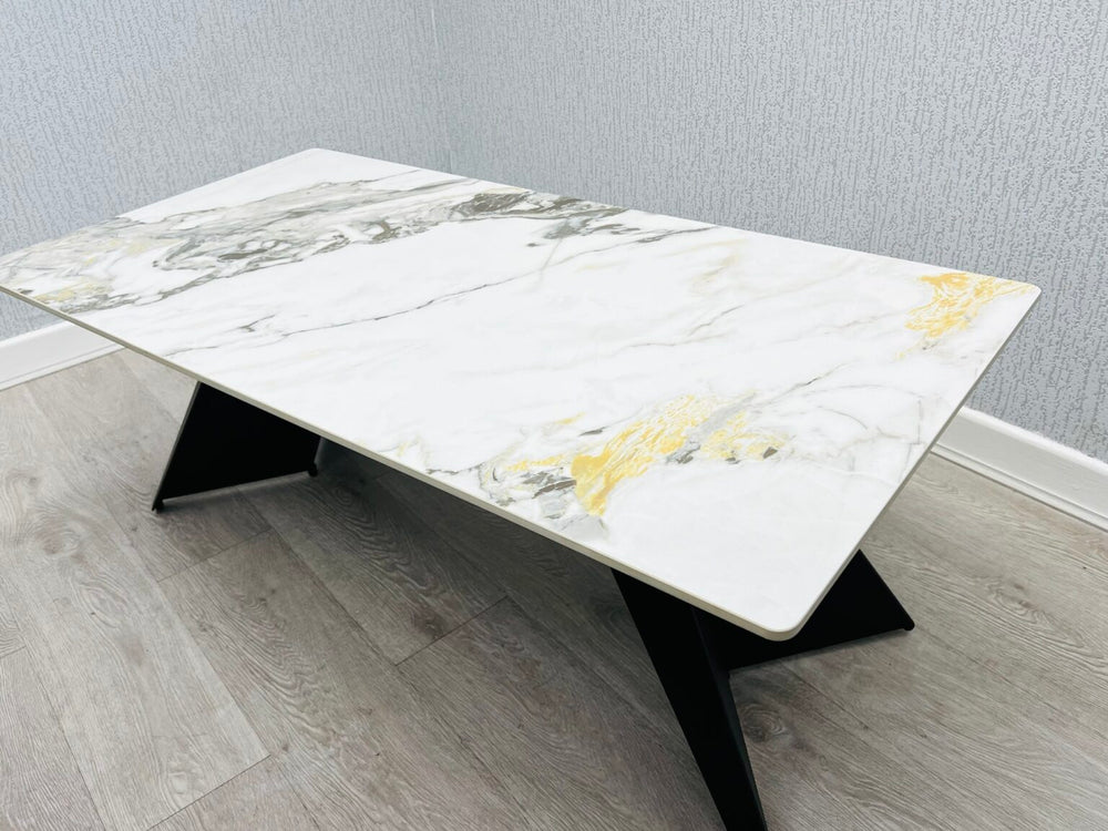 Ceramic coffee table with black legs. the ceramic top has cream and  gold colors. it is 120 cm long