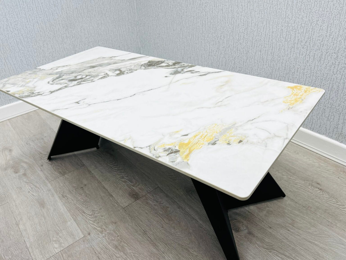 Ceramic coffee table with black legs. the ceramic top has cream and  gold colors. it is 120 cm long