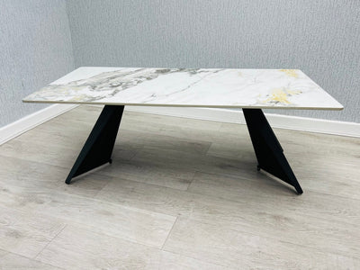 Ceramic coffee table with black legs. the ceramic top has cream and  gold colors. it is 120 cm long